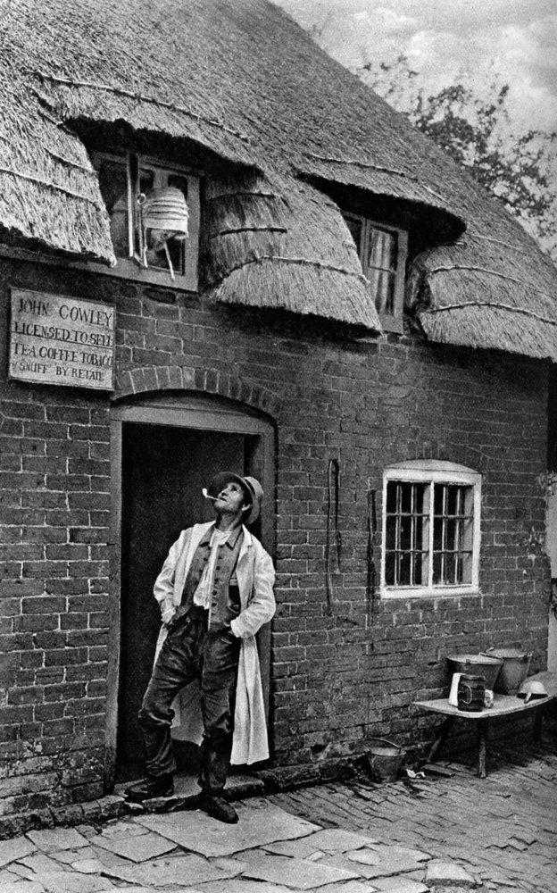 Mężczyzna palący fajkę przed sklepem, Worcestershire, ok. 1922. autorstwa A. W. Cutler