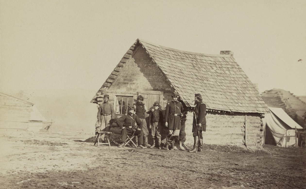 Grupa żołnierzy i dwóch młodych mężczyzn, jeden Afroamerykanin, stoją przed kwaterami z bali, 1861-65 autorstwa American Photographer