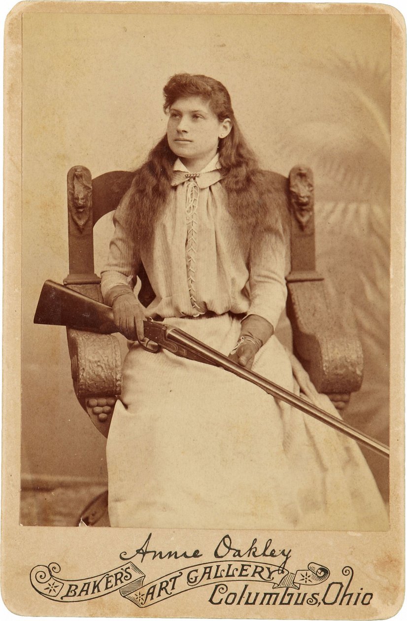 Annie Oakley: Annie Oakley:. Tutaj legendarny strzelec wyborowy siedzi raczej skromnie na masywnym krześle w stylu renesansowym, ze strzelbą spoczywającą na jej kolanach. Jej delikatne kobiece rysy i rozwiane włosy oddają jej surowość na świeżym powietrzu. autorstwa American Photographer