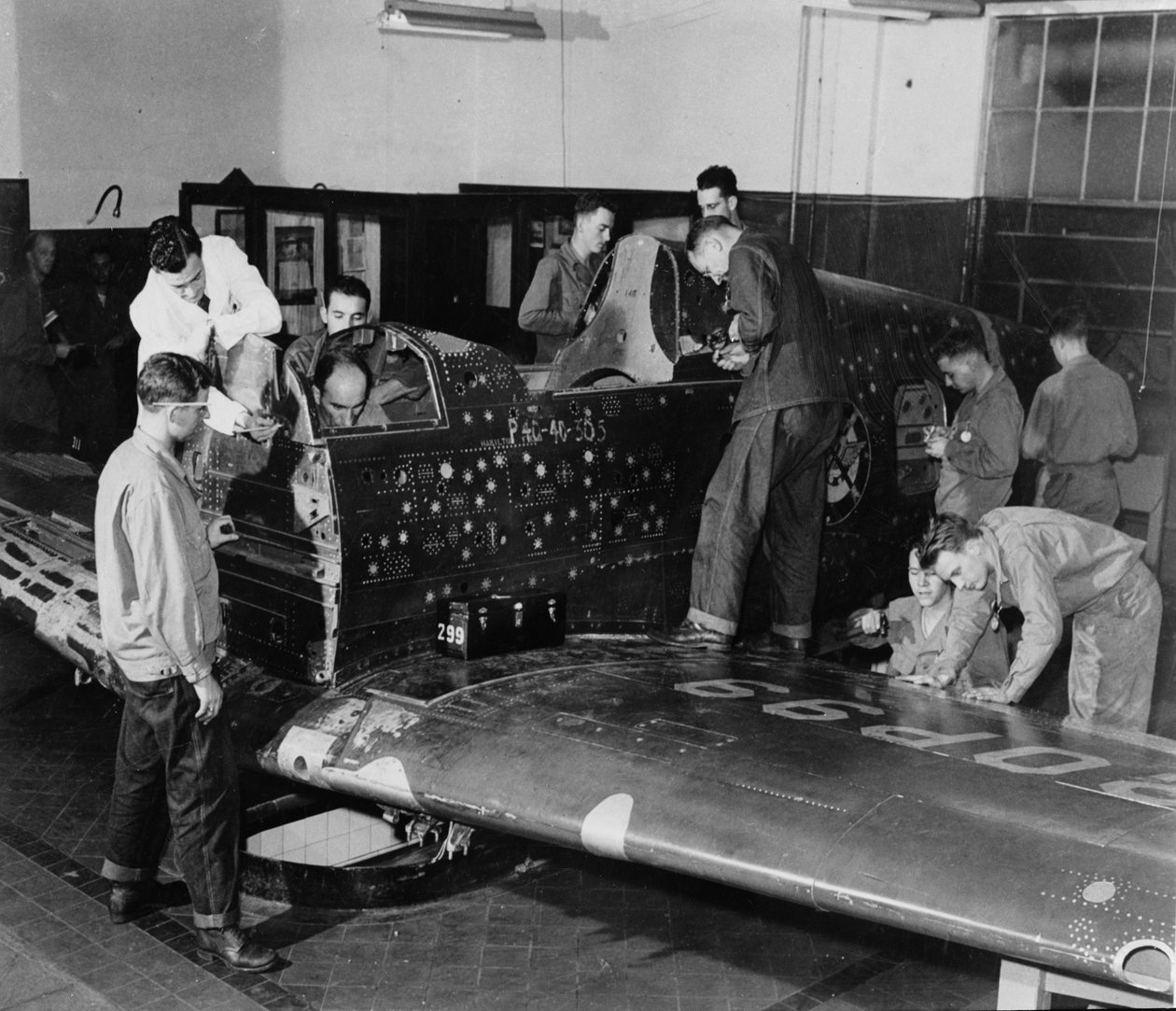 Stażyści żołnierze pracują nad „Flying Patch”, myśliwcem Curtiss „Warhawk” bez silnika i zespołu ogonowego, z symulowanymi dziurami po kulach i łatami, ok. 1942 r. autorstwa American Photographer