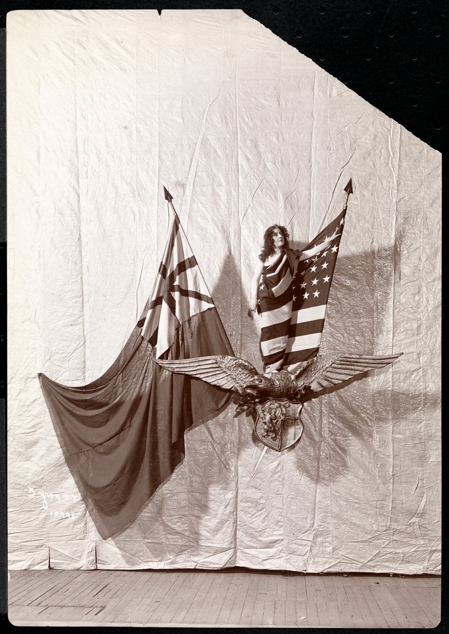 Żywy obraz: modelka udrapowana we flagę amerykańską stojąca na szczycie rzeźby łysego orła, 1900 lub 1901 (odbitka żelatynowa) autorstwa Byron Company