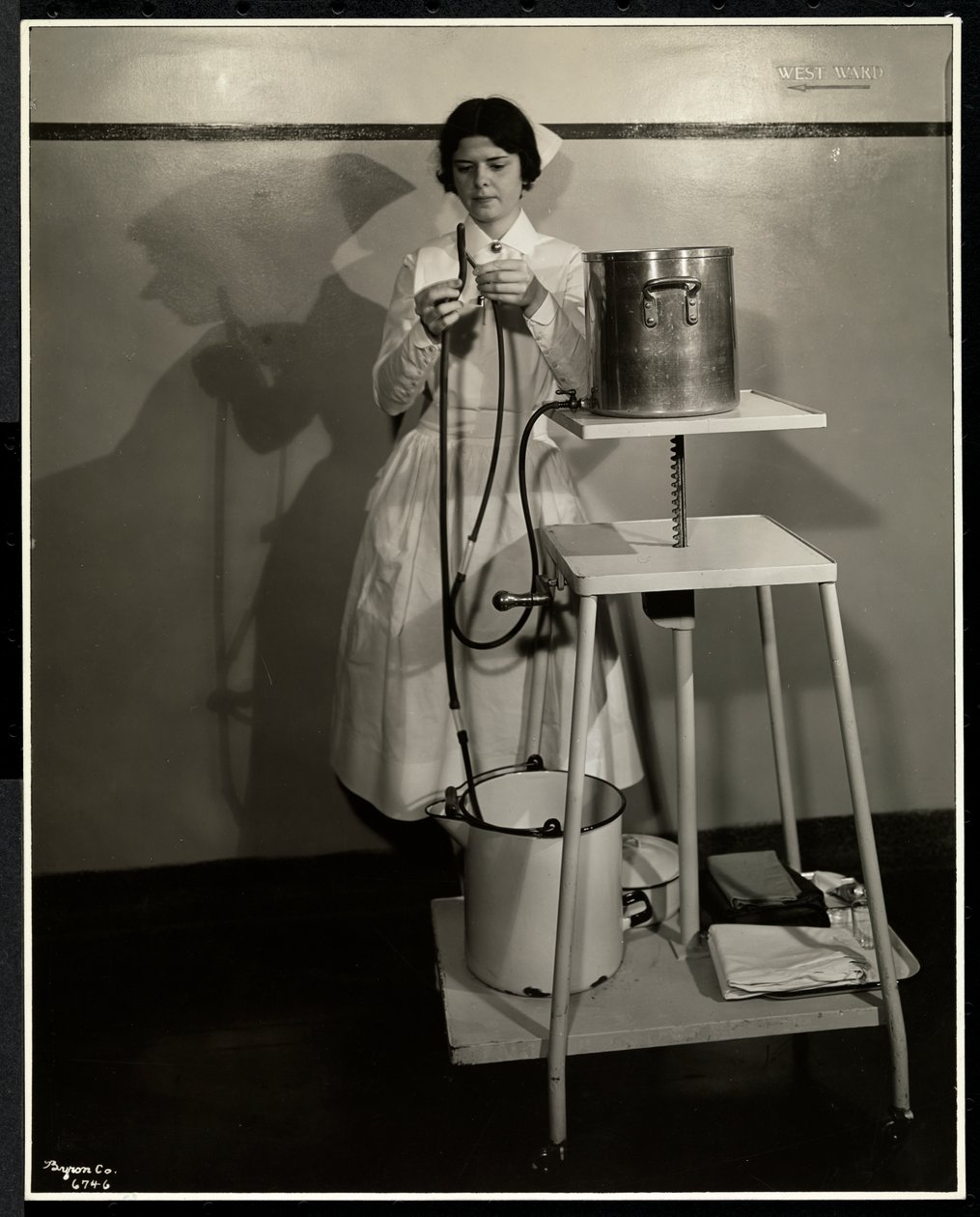 Pielęgniarka demonstruje specjalną aparaturę z rurkami i wiadrami na odpady w szpitalu Sloan Maternity, Broadway i 168th Street, Nowy Jork, 1932 (odbitka żelatynowa) autorstwa Byron Company