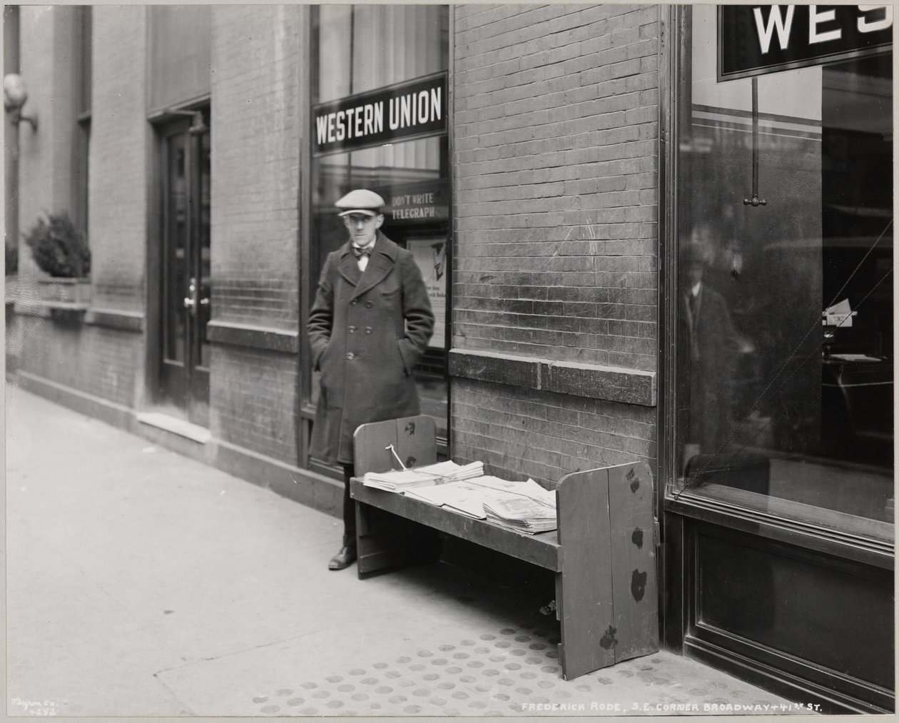 Niewidomy kioskarz, Frederick Rode, na południowo-wschodnim rogu Broadwayu i 41. ulicy. W oknie za panem Rode widać znak Western Union. autorstwa Company Byron