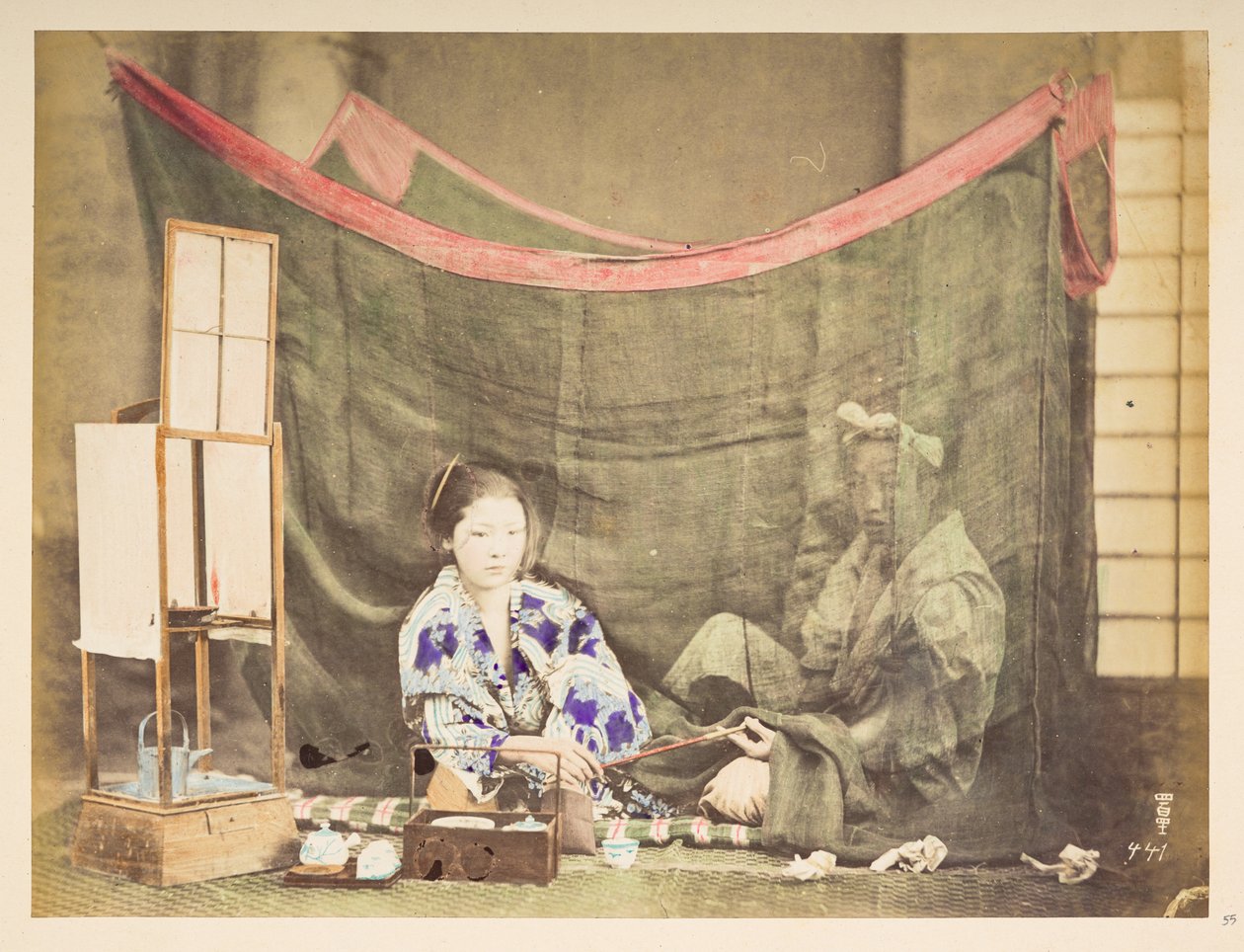 Japońska para w wolnym czasie, Studio tableau młodej Japonki, siedzącej z utrudnieniami parzenia herbaty, wręcza fajkę siedzącemu za nią mężczyźnie, osłoniętego lnianą moskitierą,   Fotograf: Nieznany  Kolekcja Lucasa: autorstwa English Photographer