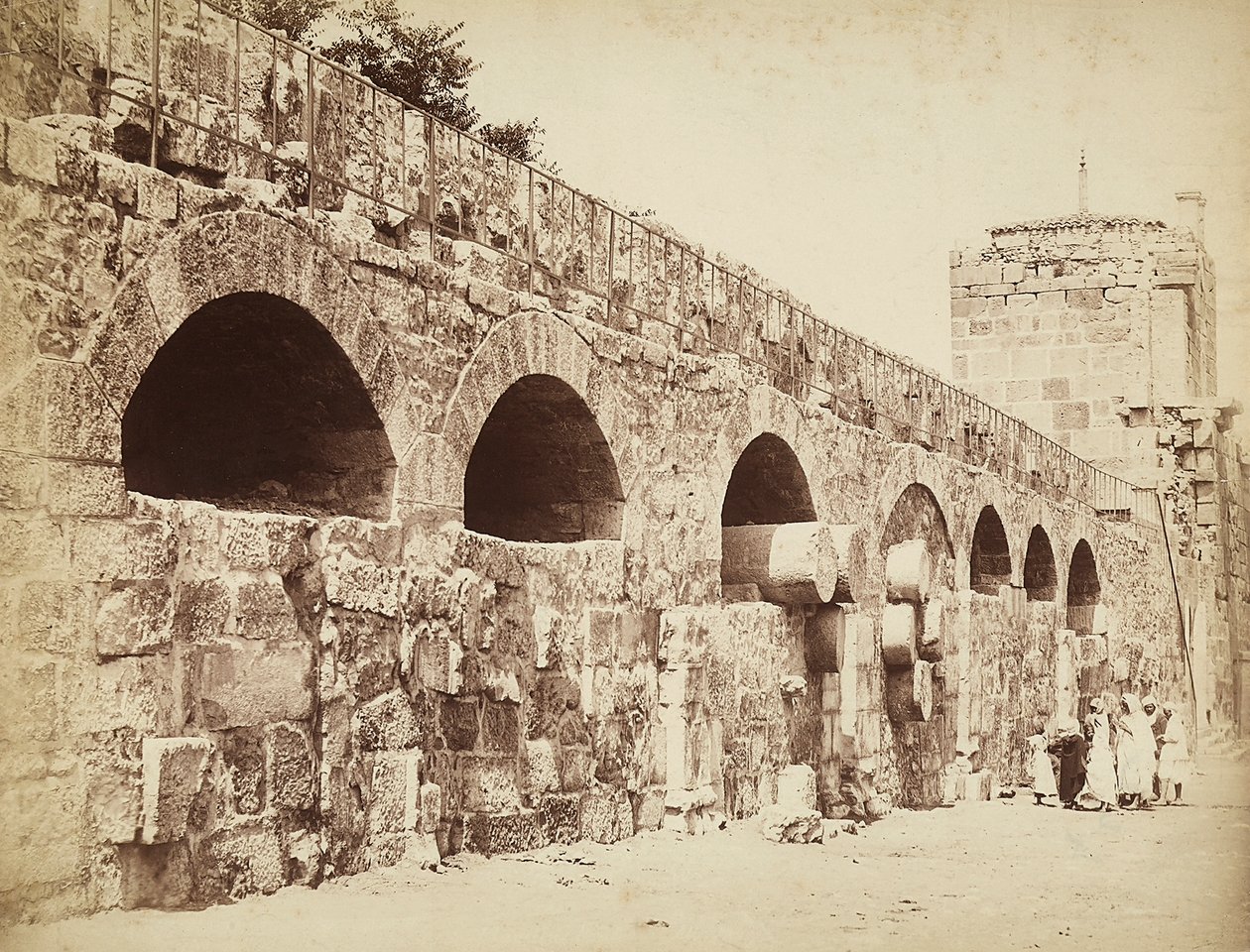 Widok na mury miejskie Heliopolis lub Baalbek, starożytne miasto syryjskie, obecnie Liban. Grupa ludzi zbiera się razem pod ścianą autorstwa Félix Bonfils