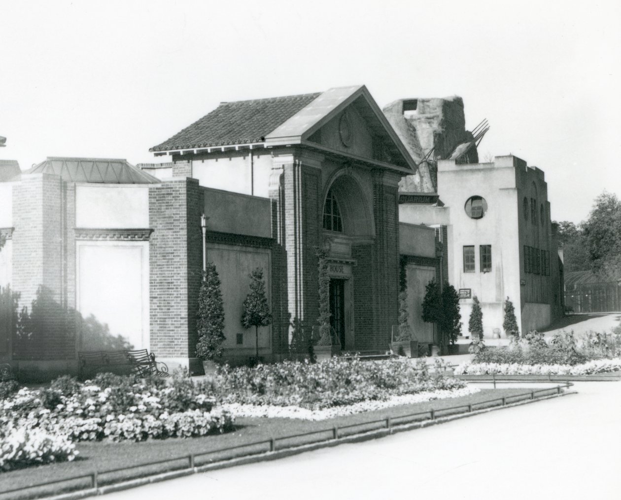 Reptile House w londyńskim zoo w 1928 roku z formalnymi klombami wzdłuż ścieżek prowadzących do wejścia (zdjęcie czarno-białe) autorstwa Frederick William Bond