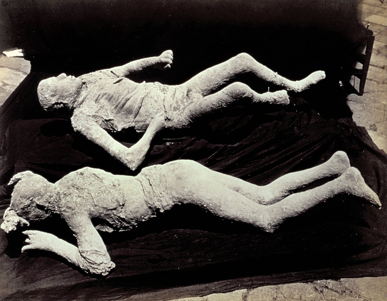 Dwa odlewy postaci ludzkich z wykopalisk w Pompejach. Eksponaty zostały umieszczone na czarnym materiale w celu ich sfotografowania autorstwa Giorgio Sommer