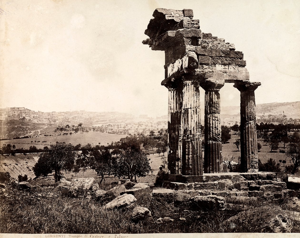 Widok na pozostałe cztery kolumny podtrzymujące belkowanie świątyni Kastora i Polluksa w Valle dei Templi, Agrigento. W tle widoczna panorama miasta autorstwa Giorgio Sommer