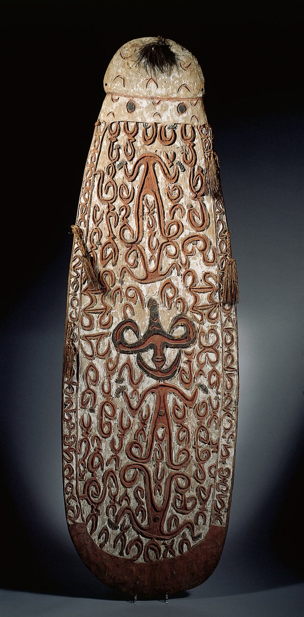 Owalna tarcza Asmat, wyrzeźbiona w reliefie z przewijanym ornamentem zawierającym wysoce stylizowane postacie, plecione frędzle do brzegu (drewno, rafia i pióra) autorstwa Guinean New