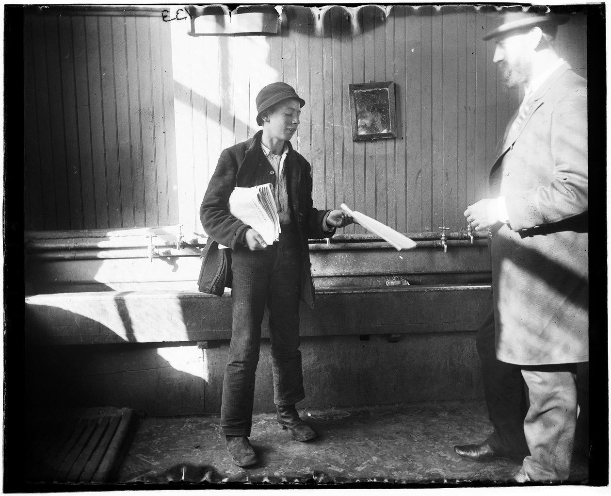 Portret gazeciarza podającego gazetę mężczyźnie w czymś, co wydaje się być toaletą w Duane Street Lodging House autorstwa Jacob August Riis