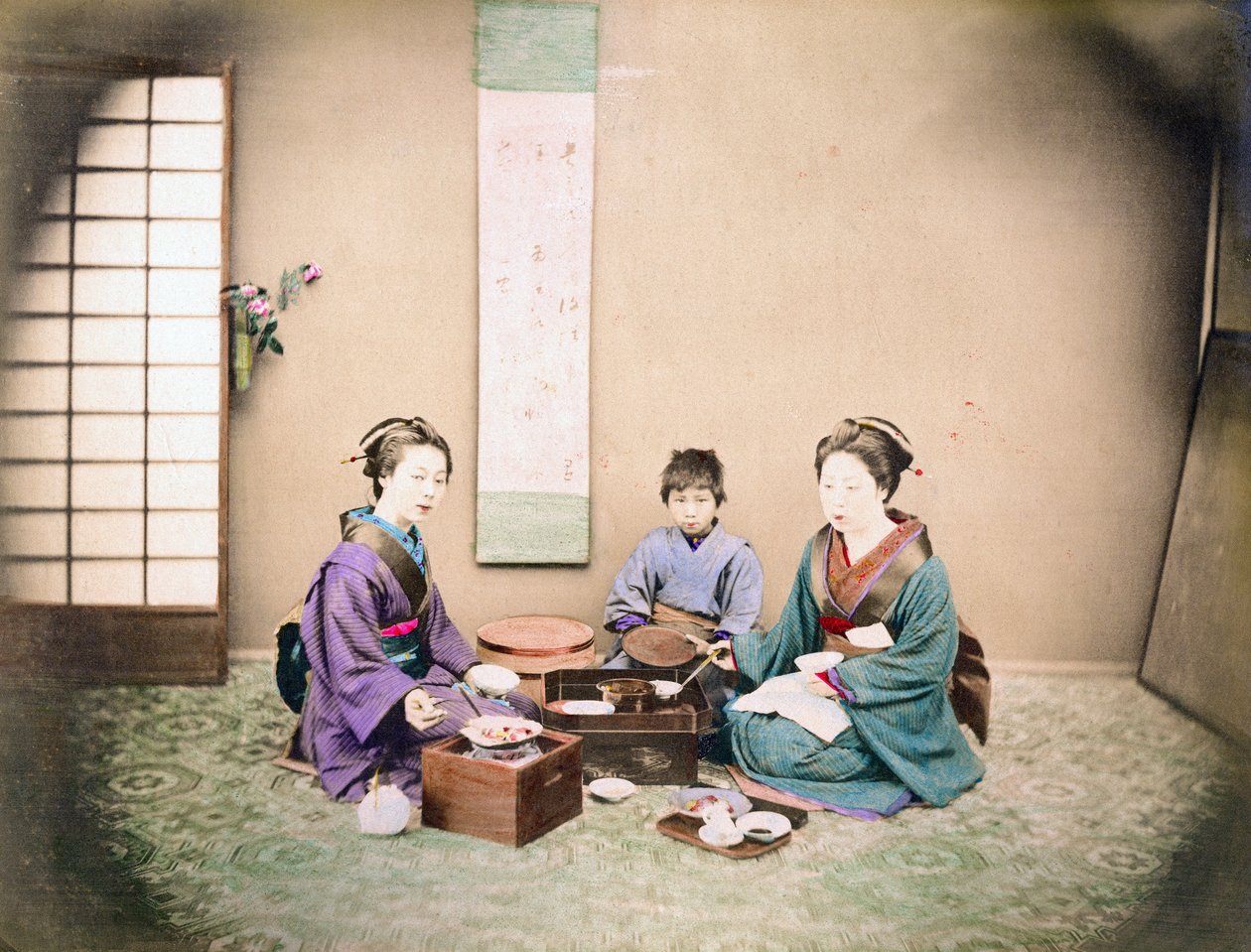 Dwie kobiety i dziecko jedzą obiad, siedząc na macie, ok. 1890 r. (zdjęcie ręcznie kolorowane) autorstwa Japanese Photographer