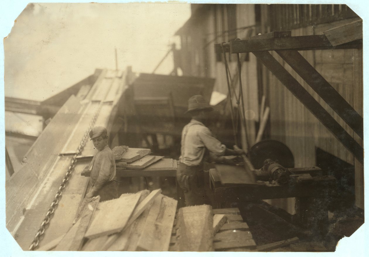 Charlie McBride lat 12 pobiera drewno z zsypu przez 10 godzin w Miller und Vidor Lumber Company, Beaumont, Texas, za co zarabia 50 centów, podczas gdy inny chłopiec piłuje je na niezabezpieczonej pile tarczowej, 191 autorstwa Lewis Wickes Hine