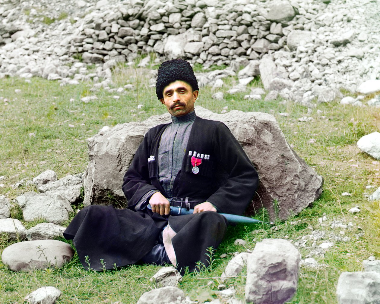 Typy dagestańskie - sunnicki muzułmanin w tradycyjnym stroju i nakryciu głowy, z zatkniętym sztyletem u boku siedzi na ziemi, Imperium Rosyjskie, między 1905 a 1915 r. autorstwa Sergey Prokudin Gorsky