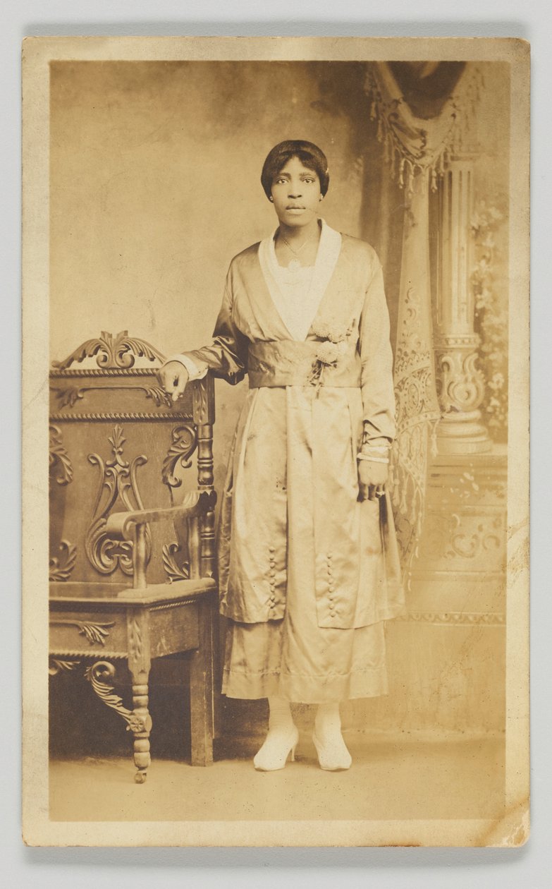 Pocztówka fotograficzna przedstawiająca kobietę stojącą przy drewnianym krześle, 1904-1918. autorstwa Unbekannt