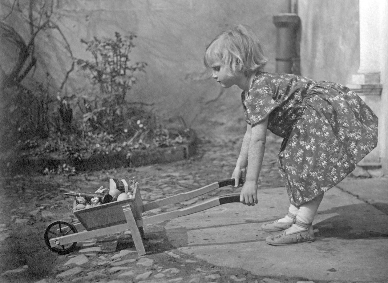 Mała dziewczynka bawi się taczką. Fotografia około 1931 autorstwa Unbekannt