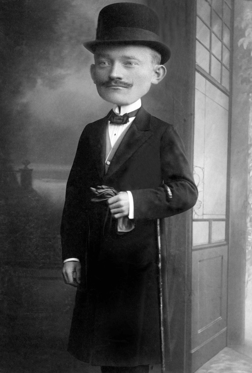 Portret bardzo eleganckiego mężczyzny z głową olbrzyma, nosi melonowy kapelusz, laskę, muszkę i czarny płaszcz. Jest to fotomontaż. Anny 1910 Historyczna fotografia, mężczyzna z gigantyczną głową autorstwa Unbekannter Künstler