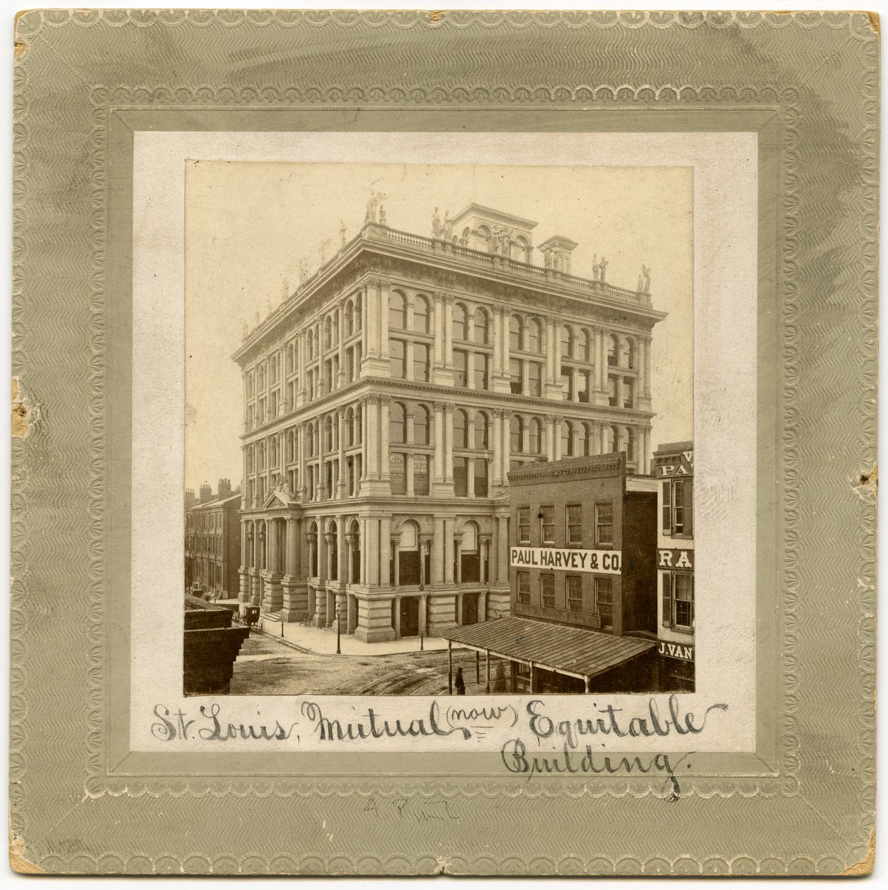 Zdjęcie sześciopiętrowego budynku z postaciami u góry. Po obu stronach widoczne są inne budynki. Budynek zwany także budynkiem St. Louis Life Insurance Building autorstwa Unknown