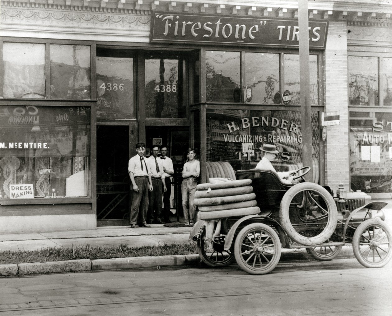 Mężczyźni i ciężarówka z oponami samochodowymi zgromadzeni przed salonem H. Bender Firestone Tire przy 4388 Olive Street autorstwa Unknown