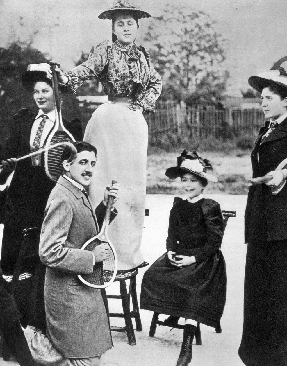 Marcel Proust pośród grupy młodych kobiet gra na gitarze na rakiecie tenisowej na Bineau Boulevard w Paryżu autorstwa Unknown photographer