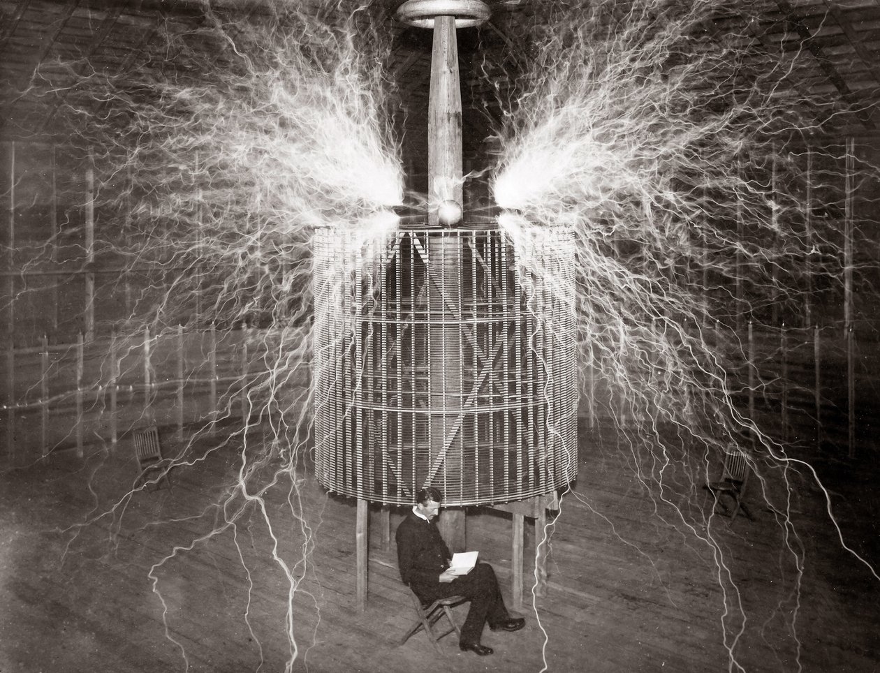 Nikola Tesla siedzący w swoim laboratorium w Colorado Springs ze swoim „nadajnikiem powiększającym” autorstwa Unknown photographer