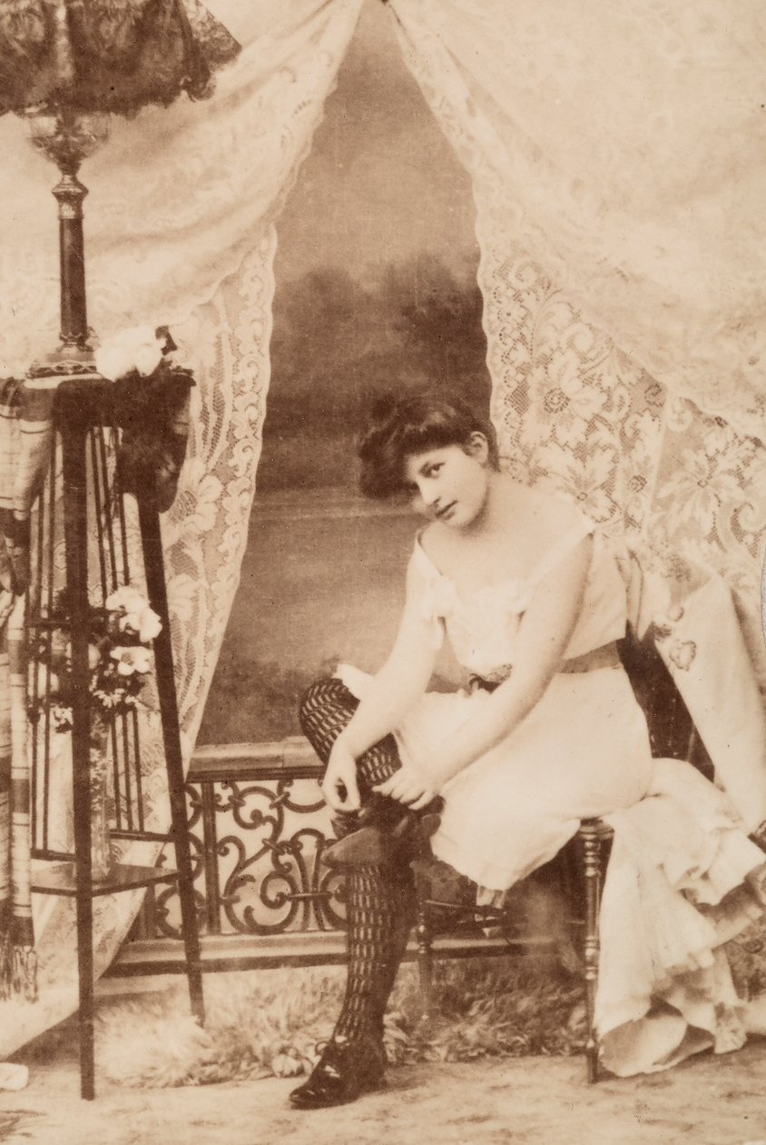 Portret młodej kobiety w intymnej odzieży, siedzącej podczas sznurowania buta. autorstwa Unknown photographer