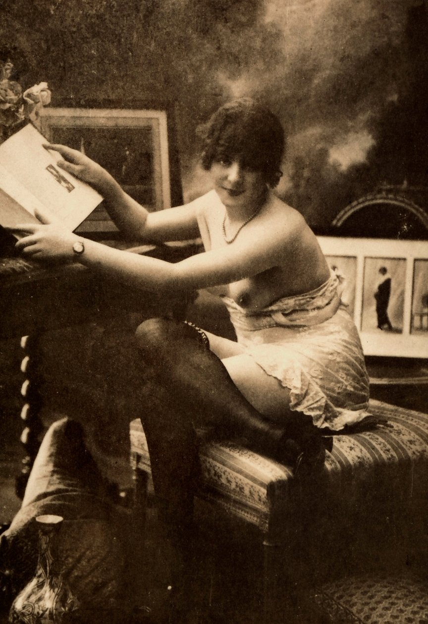 Portret młodej kobiety w intymnym stroju, siedzącej przy stole z książką. autorstwa Unknown photographer