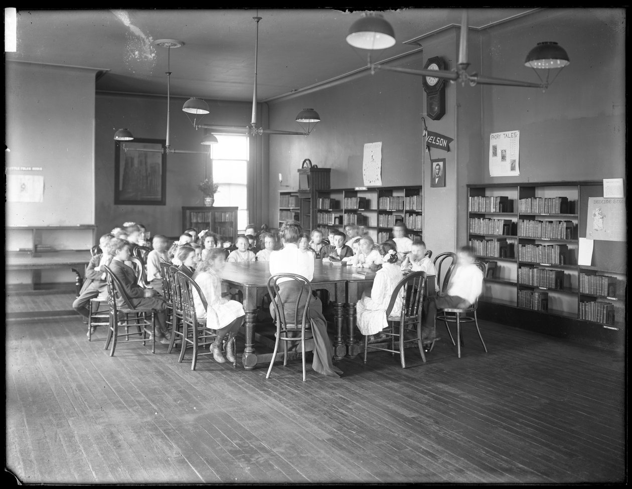 Dzieci słuchają kobiety w czytelni niezidentyfikowanej filii Biblioteki Publicznej Queens Borough, ok. 1910 (zdjęcie czarno-białe) autorstwa William Davis Hassler