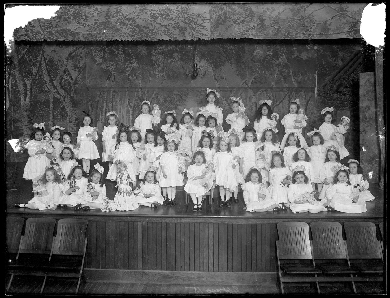 Grupa małych dziewczynek pozujących na małej scenie trzymających lalki, prawdopodobnie rzymskokatolicki azyl dla sierot, Kingsbridge, Bronx, ok. 1911 autorstwa William Davis Hassler