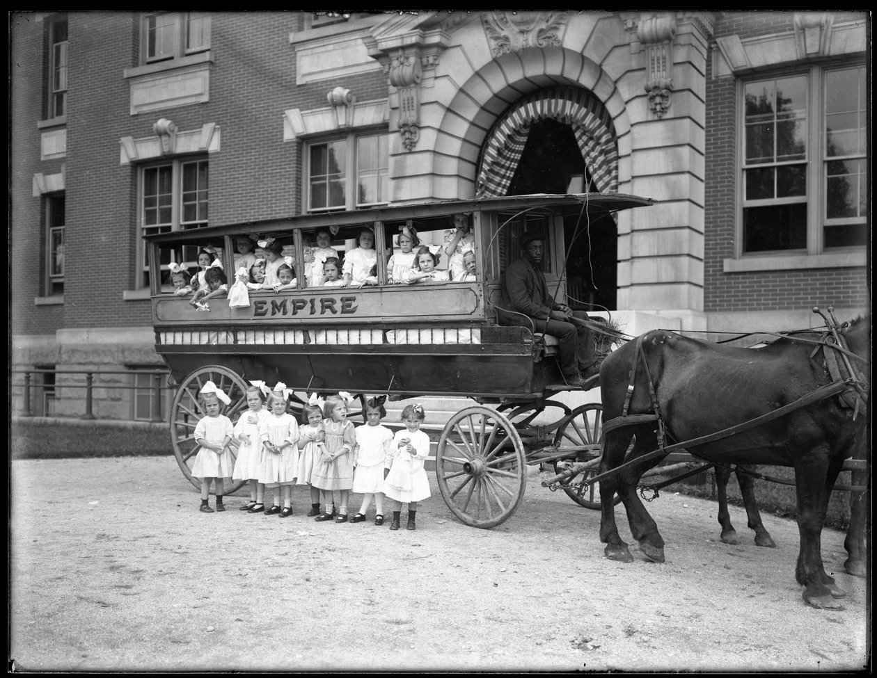 Małe dziewczynki pozują w i przed wozem ciągniętym przez konia, przed niezidentyfikowanym budynkiem, prawdopodobnie Roman Catholic Orphan Asylum, Kingsbridge, Bronx, ok. 1910 r. autorstwa William Davis Hassler