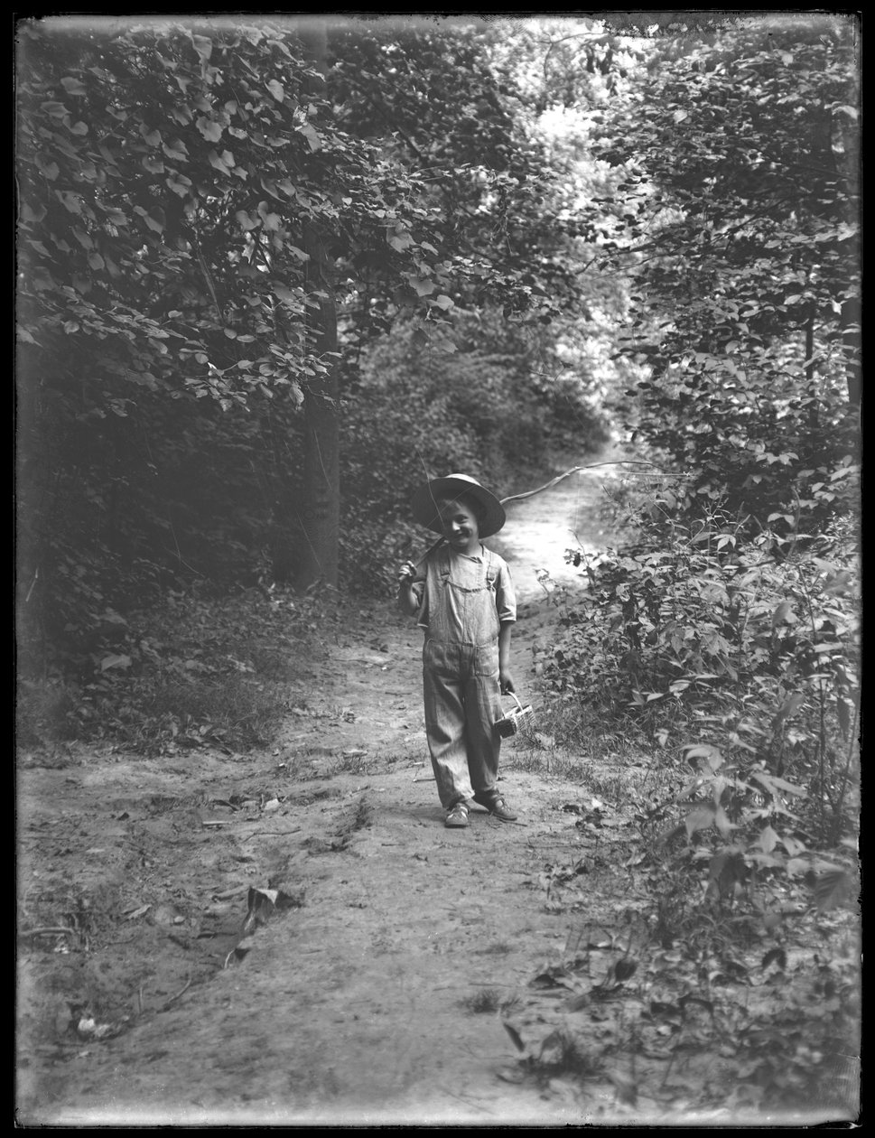 William Gray Hassler w słomkowym kapeluszu i kombinezonie, niosący wędkę i kosz, samotnie idąc ścieżką w lesie, 20 sierpnia 1911 autorstwa William Davis Hassler