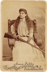 Annie Oakley: Annie Oakley:. Tutaj legendarny strzelec wyborowy siedzi raczej skromnie na masywnym krześle w stylu renesansowym, ze strzelbą spoczywającą na jej kolanach. Jej delikatne kobiece rysy i rozwiane włosy oddają jej surowość na świeżym powietrzu. autorstwa American Photographer