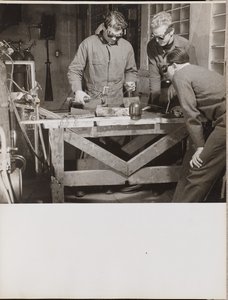 [Trzech mężczyzn w goglach spawa kawałek metalu na stole].