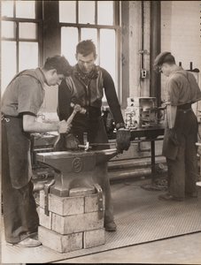 [Dwóch mężczyzn młotkuje metal na kowadle].