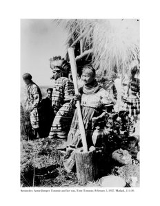 Annie Jumper Tommie używająca moździerza i tłuczka do robienia mączki kukurydzianej oraz jej syn, Tony Tommie, w czapce z orlim piórem, 5 lutego, 1927 r.