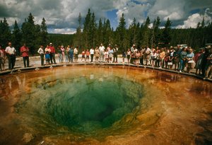 Odwiedzający park gromadzą się wokół niebiesko-zielonego basenu termalnego w kształcie kwiatu. Yellowstone Nati...
