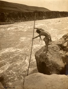 Indianin Tlakluit, stojący na skale, łowiący ryby siecią, ok. 1910 r. (zdjęcie czarno-białe) autorstwa Edward Sheriff Curtis