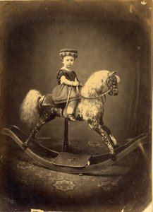 Młoda dziewczyna siedząca na bujanym koniu w kapeluszu autorstwa English Photographer