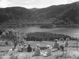 Grupa osób siedzących na trawie lub leżakach z widokiem na Thirlmere autorstwa Joseph Hardman