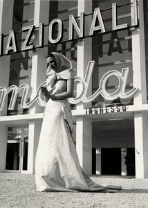Model w sukni ślubnej stworzony przez dom mody "Lamma". Artykuł charakteryzuje się nakryciem głowy w stylu klasztornym, przytrzymywanym pod szyją przez krzykliwą szpilkę w kształcie kiści winogron. (zdjęcie czarno-białe) autorstwa Luis Bogino