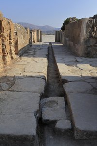 Minojskie stanowisko archeologiczne w Fajstos. Szeroki korytarz z kanałem odwadniającym za bramą skrzydła północnego otwierającym się na dziedziniec centralny i prowadzącym do dziedzińca wewnętrznego obok Apartamentów Królewskich. Fajstos, Kreta. autorstwa Minoan