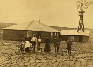 Rodzina osadników przed domem darniowym z wiatrakiem na dachu sąsiedniego budynku w hrabstwie Custer w stanie Nebraska, ok. 1885 r. (zdjęcie czarno-białe) autorstwa Solomon D. Butcher