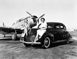 Kalifornia: 1939 Dwie kobiety siedzą na błotnikach sedana Lincoln Zephyr z 1939 roku na lotnisku z zaparkowanym za nimi samolotem jednosilnikowym (zdjęcie czarno-białe) autorstwa Unbekannt