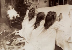 Cztery małe dziewczynki klęczące przy łóżku i odmawiające wieczorną modlitwę. autorstwa Unknown photographer