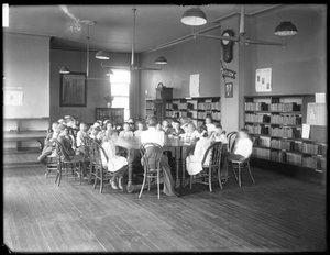 Dzieci słuchają kobiety w czytelni niezidentyfikowanej filii Biblioteki Publicznej Queens Borough, ok. 1910 (zdjęcie czarno-białe) autorstwa William Davis Hassler