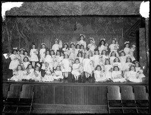 Grupa małych dziewczynek pozujących na małej scenie trzymających lalki, prawdopodobnie rzymskokatolicki azyl dla sierot, Kingsbridge, Bronx, ok. 1911