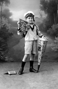 Pierwszy dzień szkoły. Młody chłopak w mundurze pozuje z tabliczką pokazującą dodatek 1+1 = 2 i niespodzianką. Fotografia około 1910 roku. autorstwa Ferdinand Georg Waldmuller