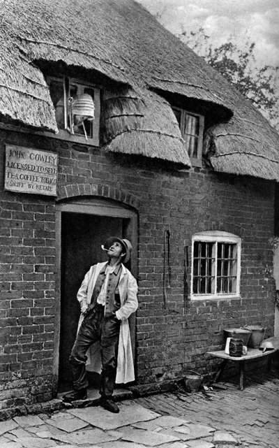 Mężczyzna palący fajkę przed sklepem, Worcestershire, ok. 1922. autorstwa A. W. Cutler