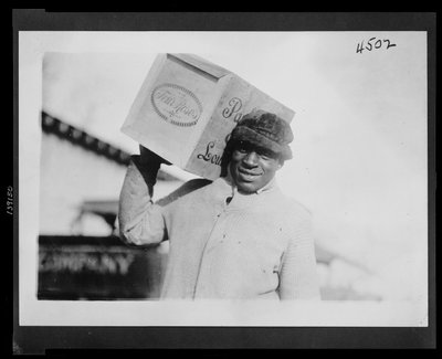 Afroamerykanin niosący na ramieniu skrzynkę whisky „Cztery róże”, prawdopodobnie skonfiskowaną przez amerykański urząd skarbowy autorstwa American Photographer