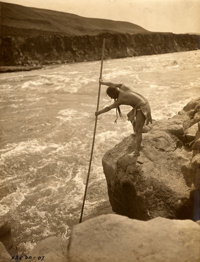Indianin Tlakluit, stojący na skale, łowiący ryby siecią, ok. 1910 r. (zdjęcie czarno-białe) autorstwa Edward Sheriff Curtis