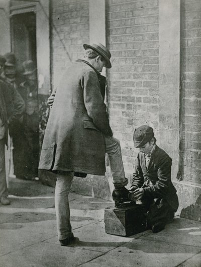 Młody pucybut lśniący męskie buty na ulicy autorstwa English Photographer